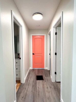 Ein Flur mit Holzboden, weißen Wänden und einer leuchtend orangefarbenen Tür.