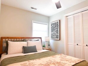 Een slaapkamer met een bed, nachtkastje, lamp, raam en kledingkast.