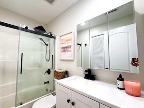 Een badkamer met een douchecabine van glas, een wit wastafelmeubel, een spiegel en een wit toilet.