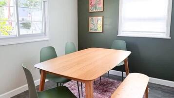Un coin repas avec une table en bois, des chaises vertes, un banc, un tapis à motifs et des œuvres d’art accrochées aux murs.