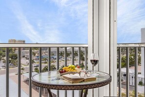 Un balcon avec une table en verre, un saladier rempli de fruits, un verre de vin rouge et une paire de lunettes.