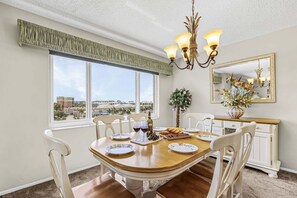 Ein Esszimmer mit großem Fenster, einer Chandelierleuchtre und einem Spiegel an der Wand.
