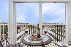 Ein Balkon mit rundem Tisch, zwei Stühlen, einer Weinflasche und einer Dessertplatte.