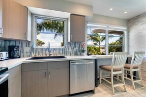 A modern kitchen with a dishwasher, a coffee maker, and a window with a view of palm trees.