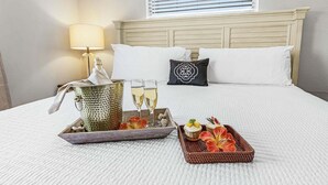 Ein ordentlich bezogenes Bett mit weißen Laken, eine Nachttischlampe sowie ein Tablett mit einer Karaffe, Gläsern und einem kleinen Servierkorb.