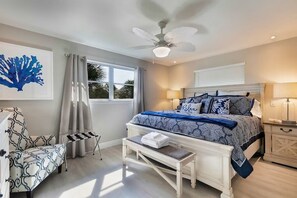 Un dormitorio con una cama, una silla, un banco, un ventilador de techo y una ventana.