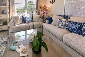 A living room with a sofa, decorative pillows, a plant, and a glass coffee table.