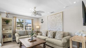 Ein Wohnzimmer mit zwei Sofas, einem Couchtisch, einem Fernseher, einem Deckenventilator und einem großen Fenster.