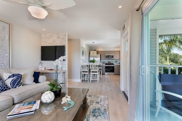 A modern living room with a sofa, coffee table, and decorative items. A kitchen is visible in the background with a dining area.