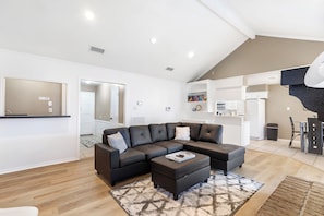 A modern living room with a sectional sofa, ottoman, and a dining area with a table and chairs.