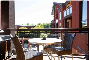 Ein Balkon mit Korbstühlen, einem runden Tisch und einem Grill.