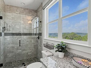 Une salle de bain avec une douche, des toilettes, un lavabo et une fenêtre donnant sur un beau paysage.
