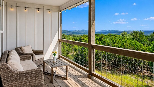Un espacio al aire libre techado con muebles de mimbre, una mesita y vistas a un paisaje verde.