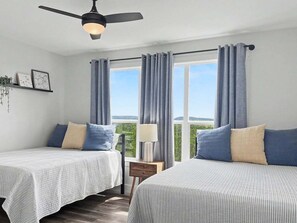 A room with two beds, a ceiling fan, a window with curtains, a bedside table, and a view of greenery. - Sunrise Social - Modern, Views, Ping Pong, Games (Canyon Lake)