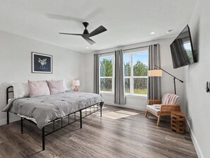 A bedroom with a bed, a ceiling fan, a TV, and a window with curtains.