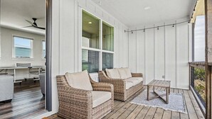 Un porche cubierto con muebles de mimbre, una pequeña mesa y vista al interior.