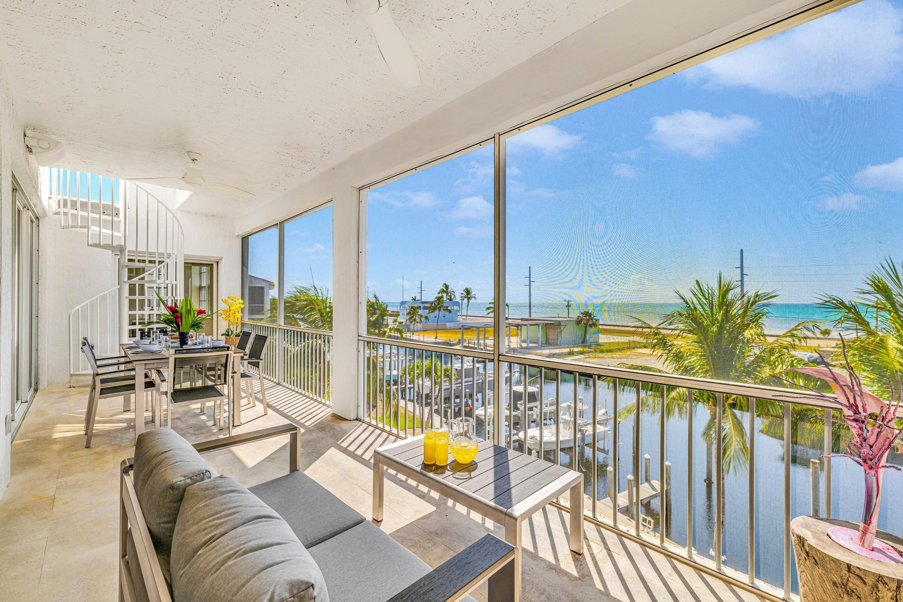 Un balcone con vista sul mare, una zona pranzo con posti a sedere all'aperto e una scala che conduce a un piano superiore.
