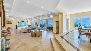 Een ruime woonkamer met een grote televisie, comfortabele zithoek en uitzicht op de oceaan.