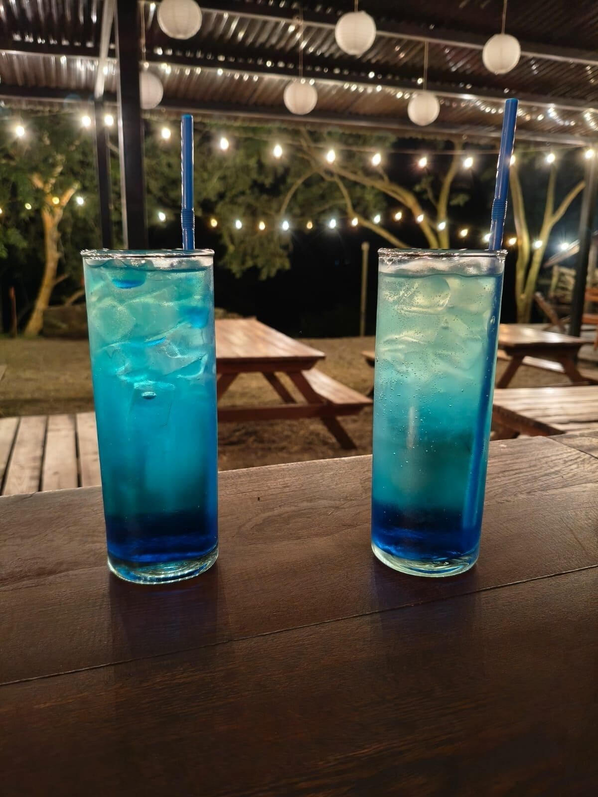 Two tall glasses of blue beverage with straws on a wooden table.