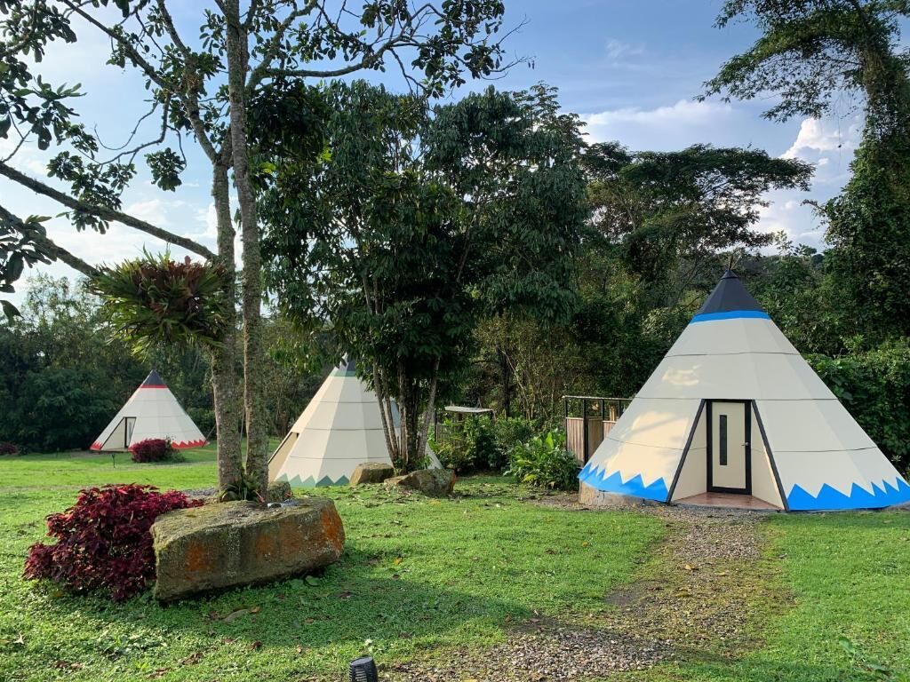Um camping com várias barracas cônicas, uma área gramada e árvores.