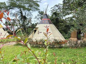 A teepee with a conical roof, surrounded by a grassy area with trees and a small wooden structure. - Refugio Natural Destino Payacal (La Mesa)