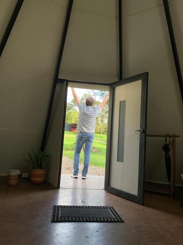 A person exiting a tent-like structure with a door, a potted plant, and a doormat on the floor.