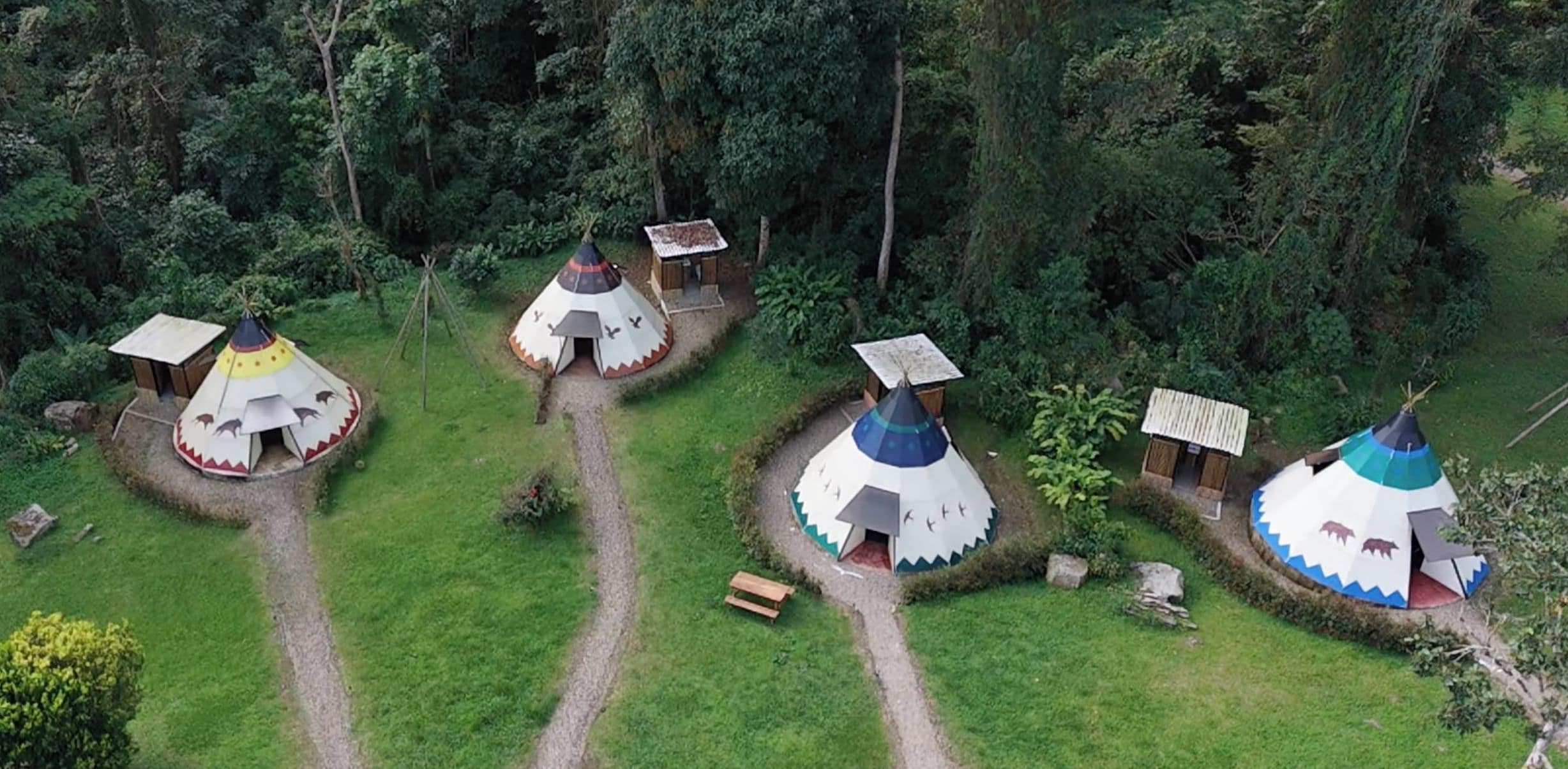 Un grupo de yurtas con un sendero de tierra que las conecta, rodeadas de un bosque denso.