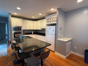 A modern kitchen with white cabinets, a black countertop, and a built-in island with bar stools. - A'Boat Time-3 BR, 3 BA, beach retreat with backyard, 3 min walk to beach (Kure Beach)