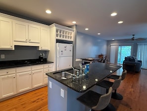 A modern kitchen with white cabinets, a black countertop, and a central island with bar stools. - A'Boat Time-3 BR, 3 BA, beach retreat with backyard, 3 min walk to beach (Kure Beach)