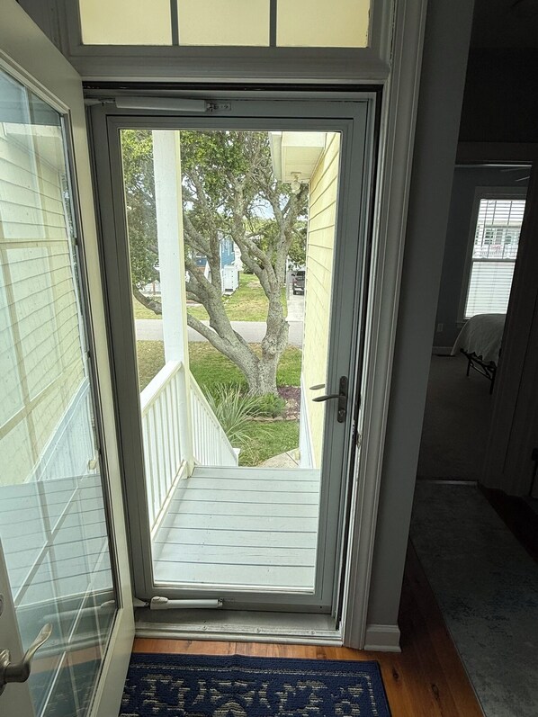 A view through a glass door leading to a porch with a wooden railing, a tree, and a lawn. - A'Boat Time-3 BR, 3 BA, beach retreat with backyard, 3 min walk to beach (Kure Beach)