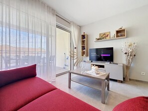 Ein modernes Wohnzimmer mit einer Couch, einem Couchtisch, einem Fernseher und einer Schiebetür zu einem Außenbereich.