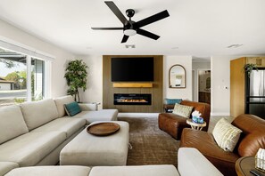 Una sala de estar moderna con chimenea, ventilador de techo y televisor grande.