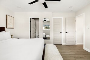 Une chambre Ă coucher comprenant un lit, un ventilateur de plafond, une porte donnant sur un placard et un couloir.