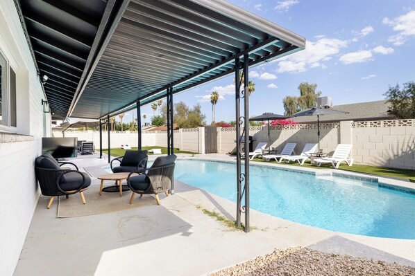 Un espacio al aire libre cubierto con piscina, sillas de descanso y una chimenea.