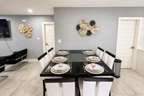 A dining area with a rectangular table set for six, white chairs, a black table, and a grey wall with decorative wall art. - Perfect 4-bedroom mid-century home in Grand Prairie (Grand Prairie)