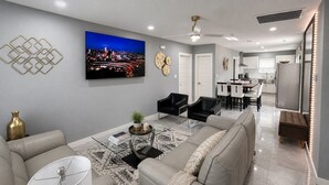 A modern living room with a sofa, chairs, a coffee table, and a TV on the wall. - Perfect 4-bedroom mid-century home in Grand Prairie (Grand Prairie)
