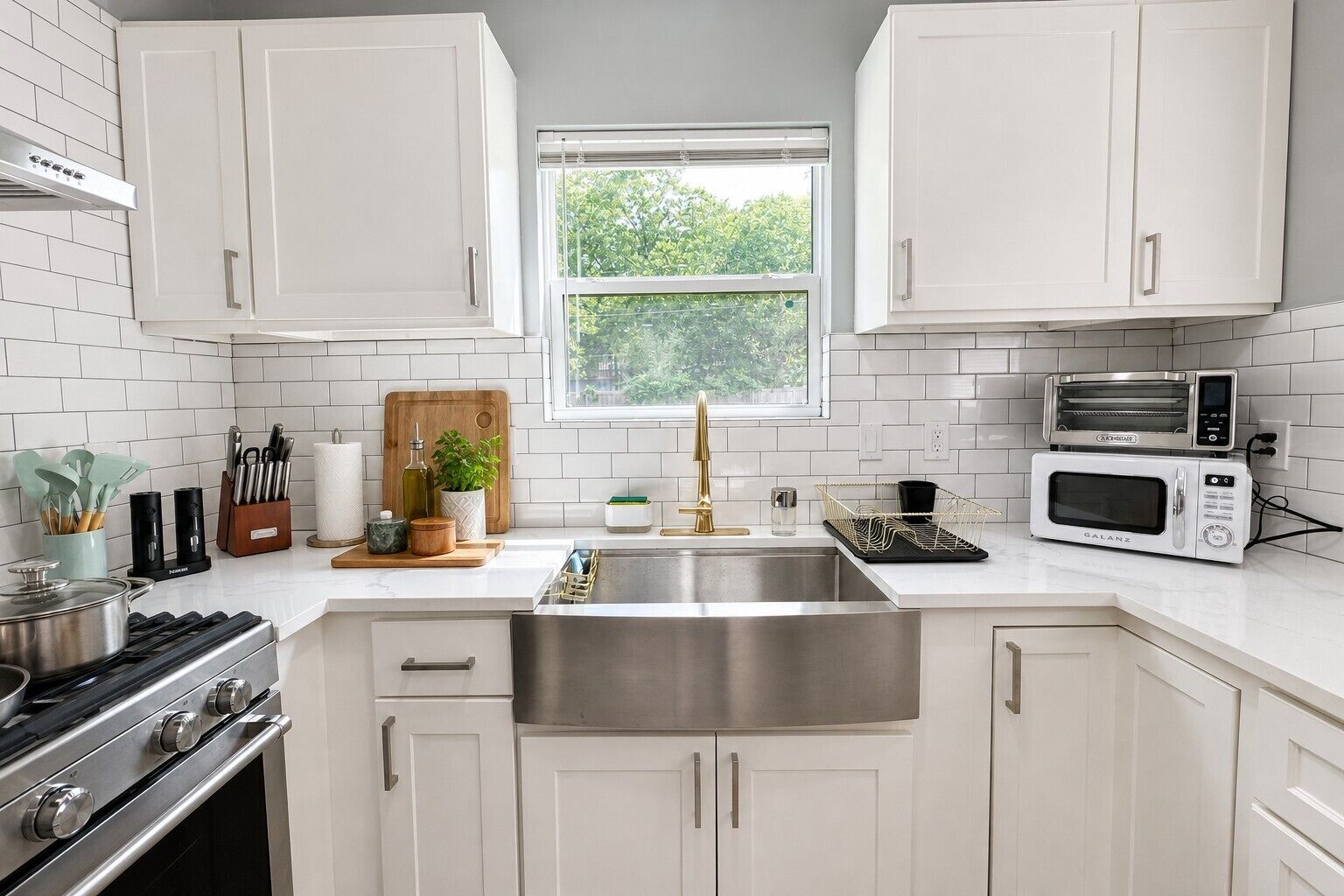A modern kitchen with white cabinets, stainless steel appliances, and a window providing natural light.