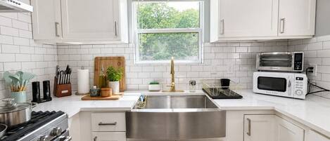 A modern kitchen with white cabinets, stainless steel appliances, and a window providing natural light.
