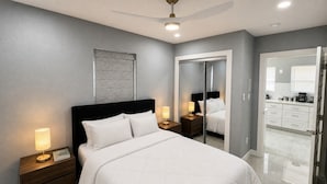 A modern bedroom with a bed, bedside tables, a ceiling fan, and a bathroom visible through an open door. - Perfect 4-bedroom mid-century home in Grand Prairie (Grand Prairie)
