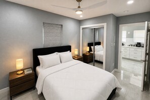 A modern bedroom with a bed, bedside tables, a ceiling fan, and a bathroom visible through an open door. - Perfect 4-bedroom mid-century home in Grand Prairie (Grand Prairie)