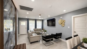 A modern living room with a sofa set, a coffee table, and a dining area with chairs and a table. - Perfect 4-bedroom mid-century home in Grand Prairie (Grand Prairie)