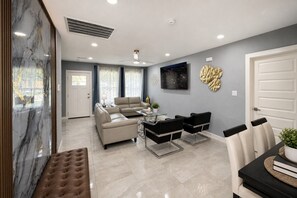 A modern living room with a sofa set, a coffee table, and a dining area with chairs and a table. - Perfect 4-bedroom mid-century home in Grand Prairie (Grand Prairie)