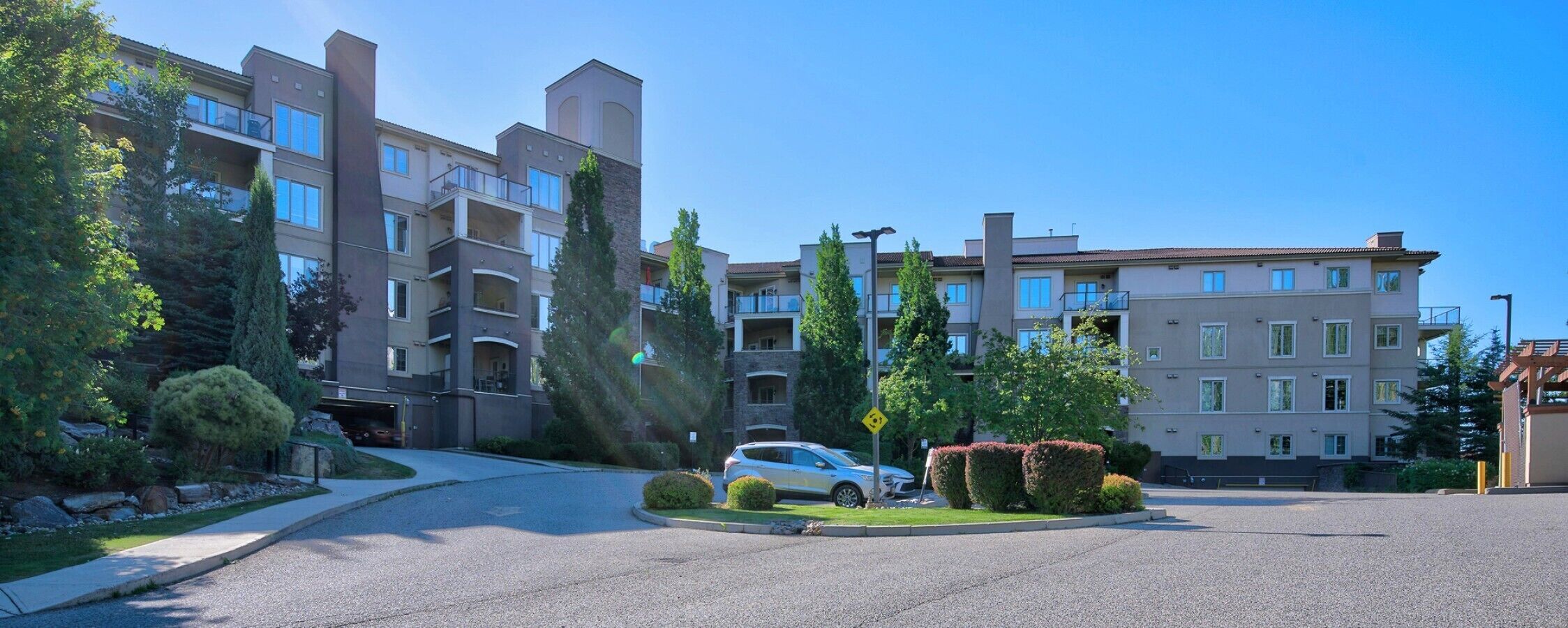 A multi-story residential building with balconies, a parking area, and well-maintained landscaping.