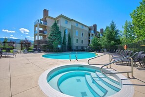 A swimming pool with steps, lounge chairs, and a building with balconies. - Mountain View 3 Bd | Pool, Hot Tub & Golf 2208 (Kelowna)