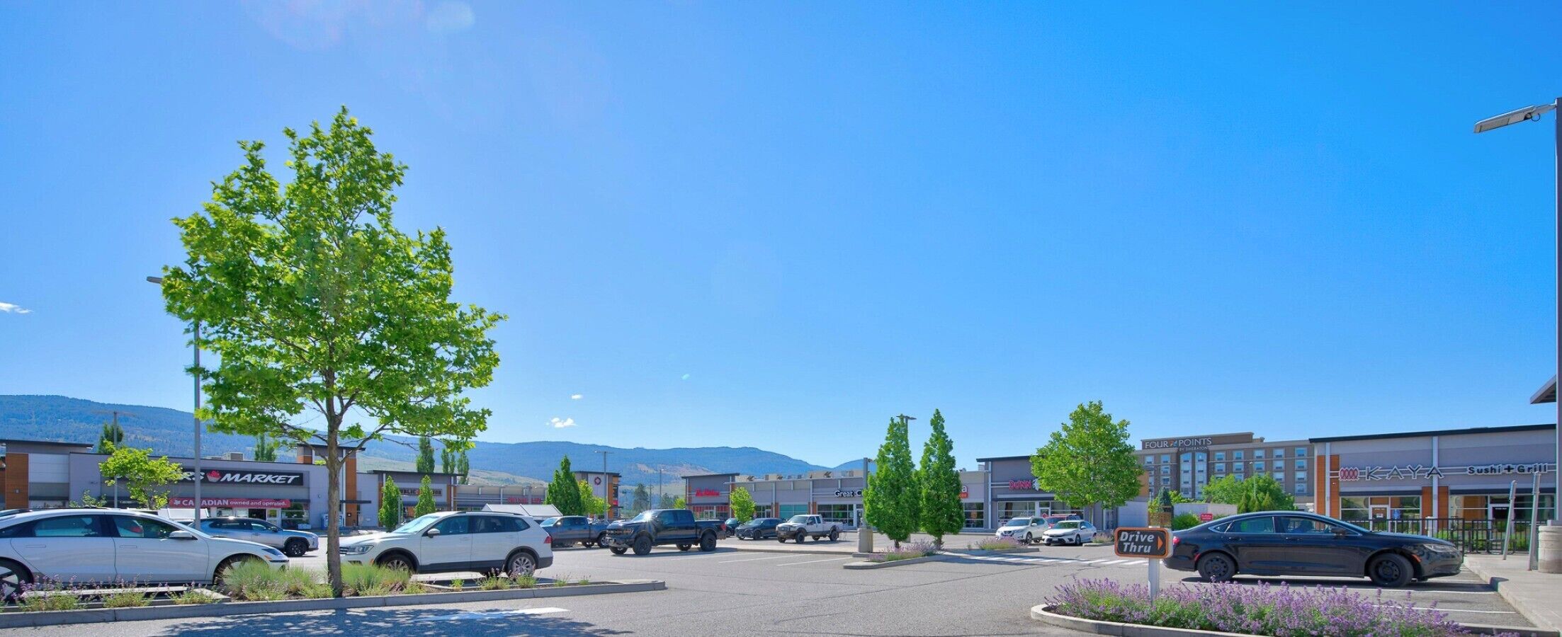 Un parking rempli de voitures, un service au volant et divers commerces, notamment une épicerie et un restaurant de sushis.