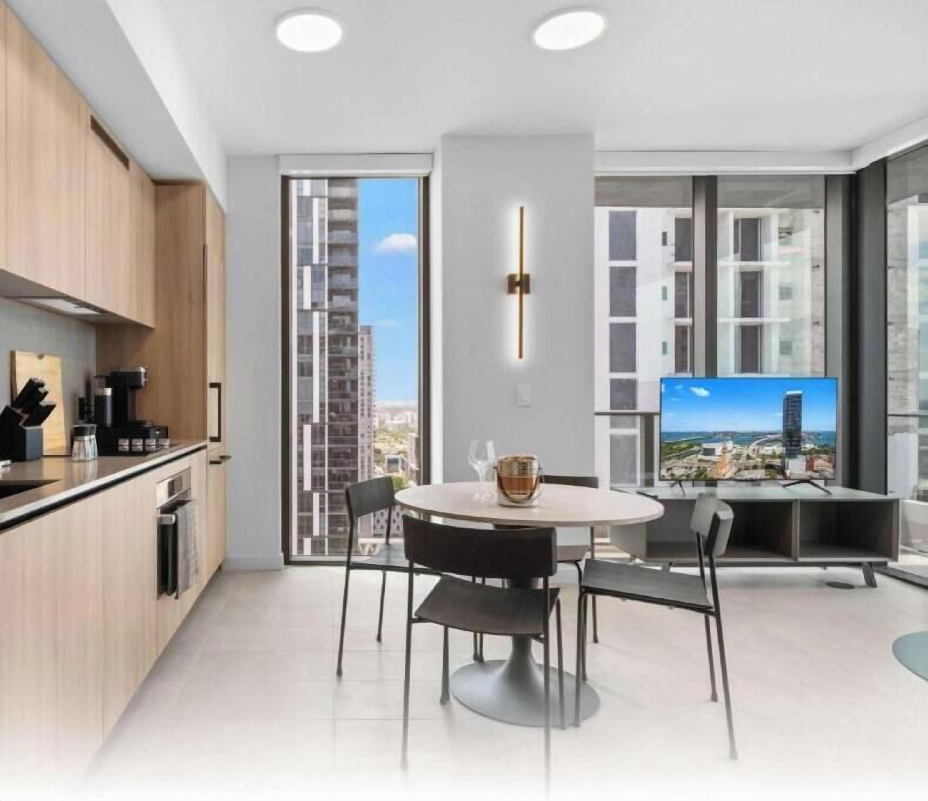 A modern kitchen with a dining area, large windows, and a view of a cityscape.