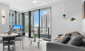 Ein modernes Wohnzimmer mit einer Couch, einem Esstisch und einem Balkon mit großen Fenstern.