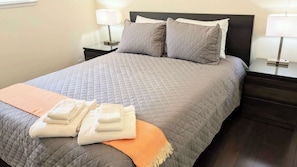 A neatly made bed with a quilted cover, two pillows, a folded blanket, and a striped throw.