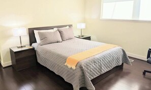 Een slaapkamer met een bed, twee nachtkastjes, een lamp op elk kastje, een raam en een deur.