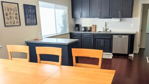 Een moderne keuken met donkere kastjes, een koffiezetapparaat en een vaatwasser. Er is een eethoek met een houten tafel en stoelen.